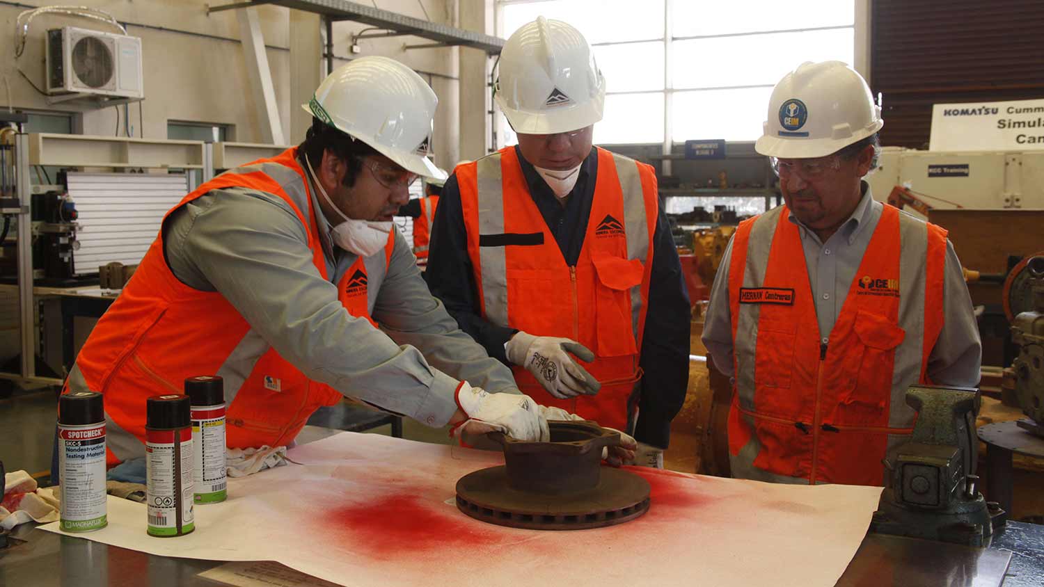 Three employees looking at part on a workbench