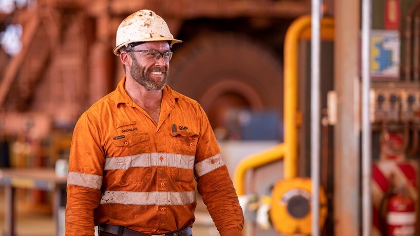 Man in BHP orange uniform shirt with grease stains pictured working in workshop