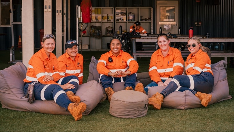 Group of women working at BHP in orange shirts sitting down on cushions and smiling