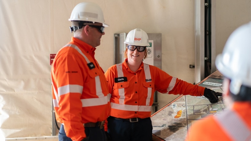 Man and woman working at BHP Jansen with orange shirt and hats pointing at project plans