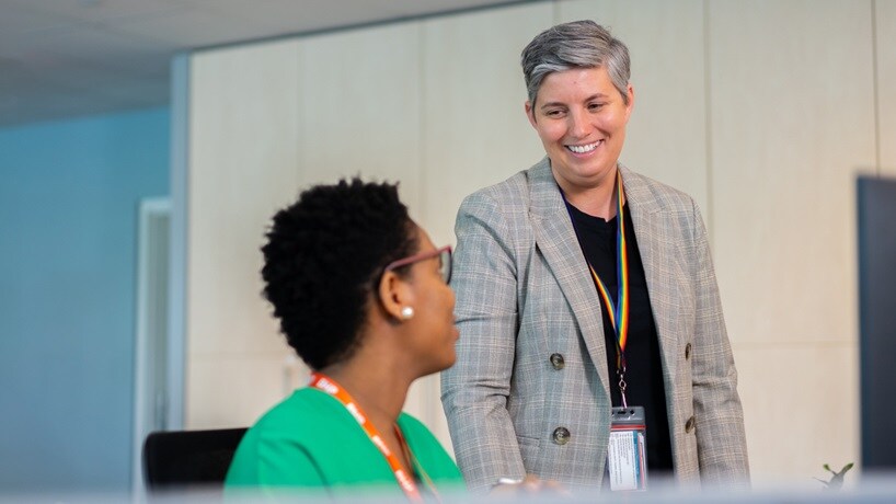Two women shown in office environment with BHP lanyards smiling at each other