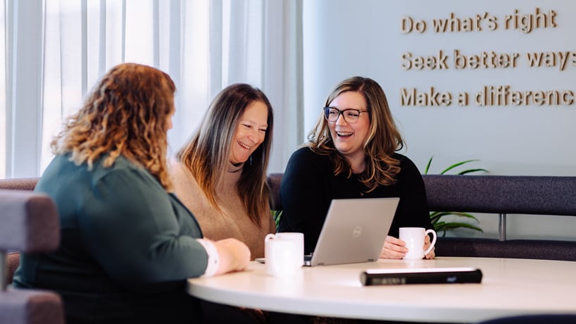 Two women shown in office environment with BHP lanyards smiling at each other
