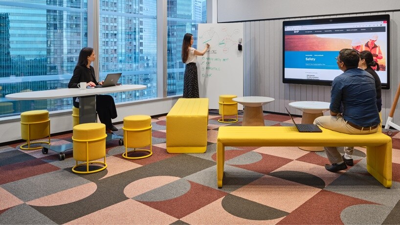 Office workshop room shown with people brainstorming ideas on the whiteboard and yellow seats and whiteboards in city backdrop