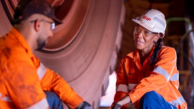 Man and woman smiling in BHP orange PPE seen working on a tyre in Newman
