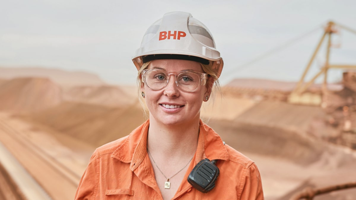 Kayla smiling and iron ore landscape and mine shown in background