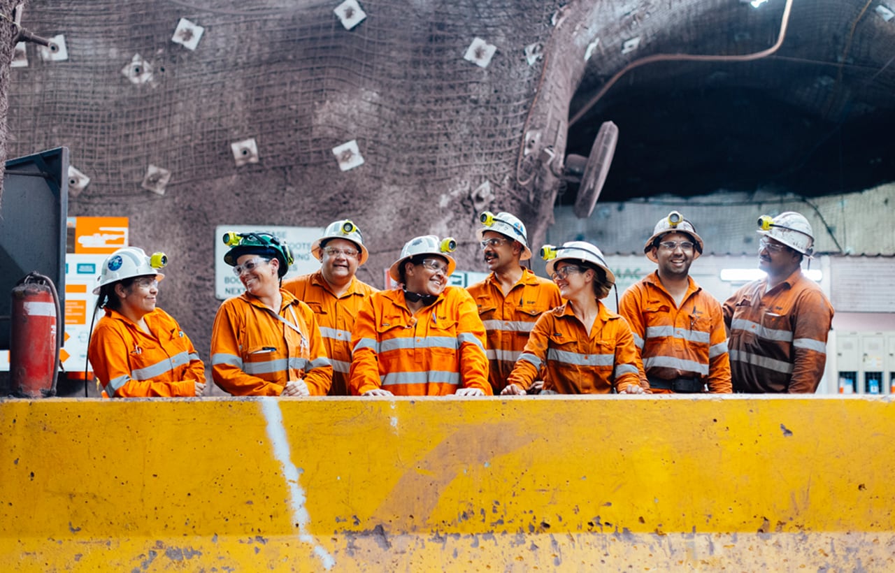 A group of workers in hi-vis look at each other happily underground