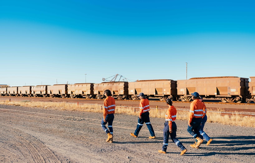 Four workers walking along a dirt track with a locomotive in the background