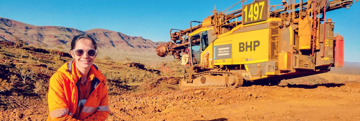 woman on mine site smiling to camera with equipment in the background
