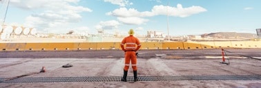 man with back to camera in mining uniform looking at a mine site