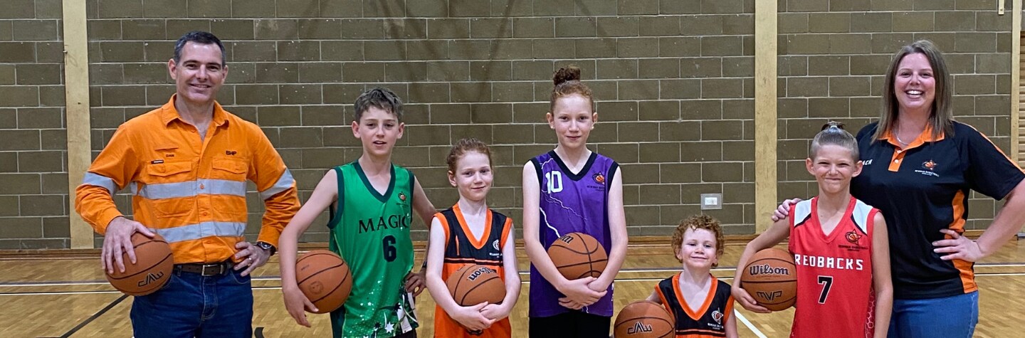 kids on basketball court with man in mining uniform holding a basketball smiling to camera
