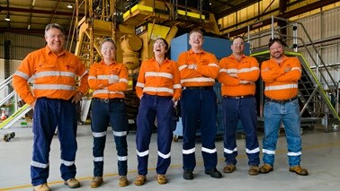 People smiling and laughing wearing BHP orange shirts with machinery in the background