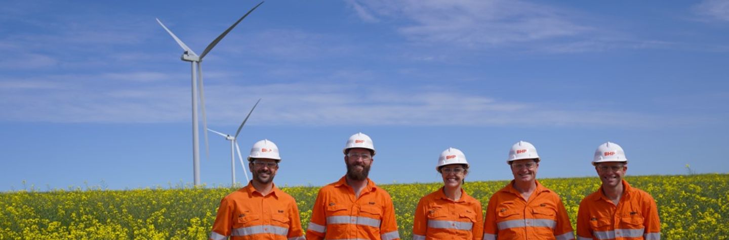 five BHP employees in hardhats smiling with wind farm background