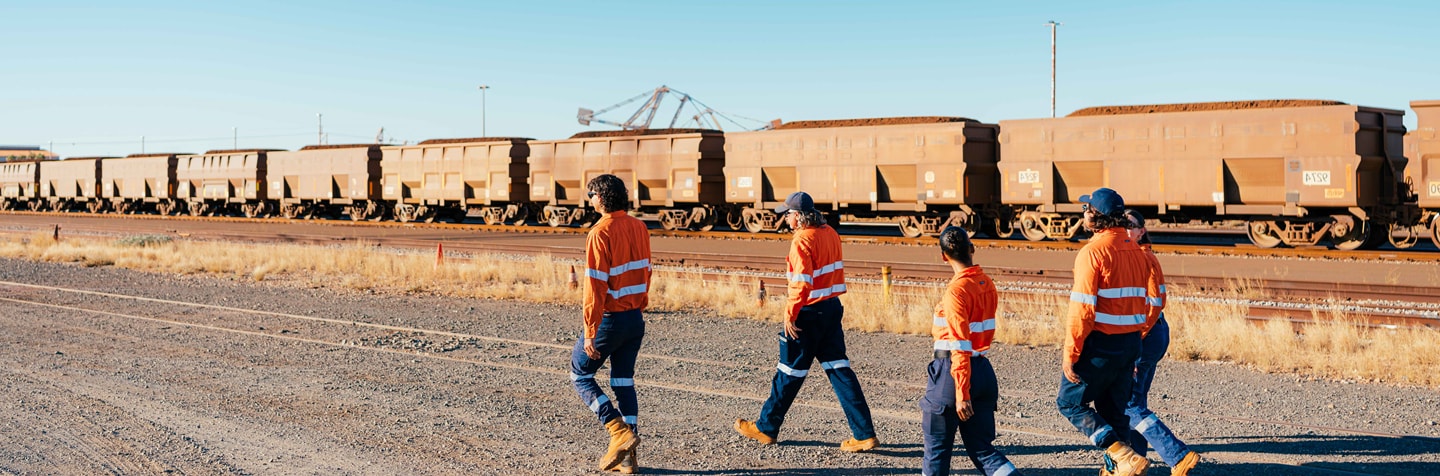 Four workers walking on dirt track with a locomotive in the background