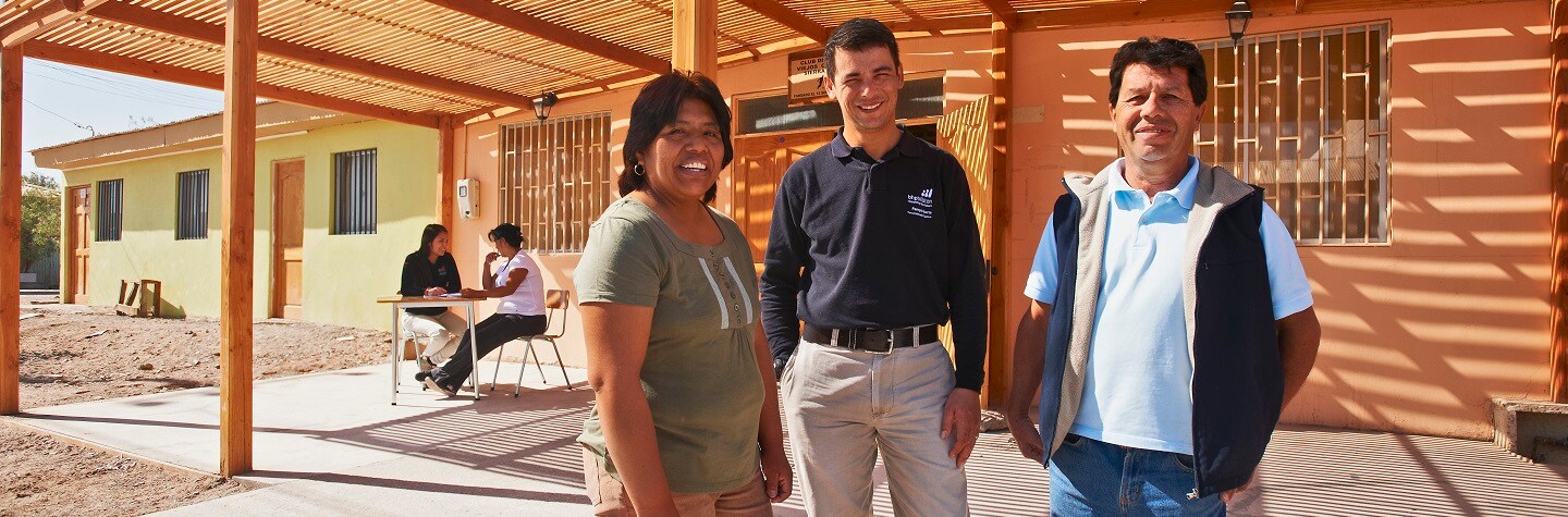 Three people, two men and a woman, stand outside in a semi-circle smiling at the camera. 