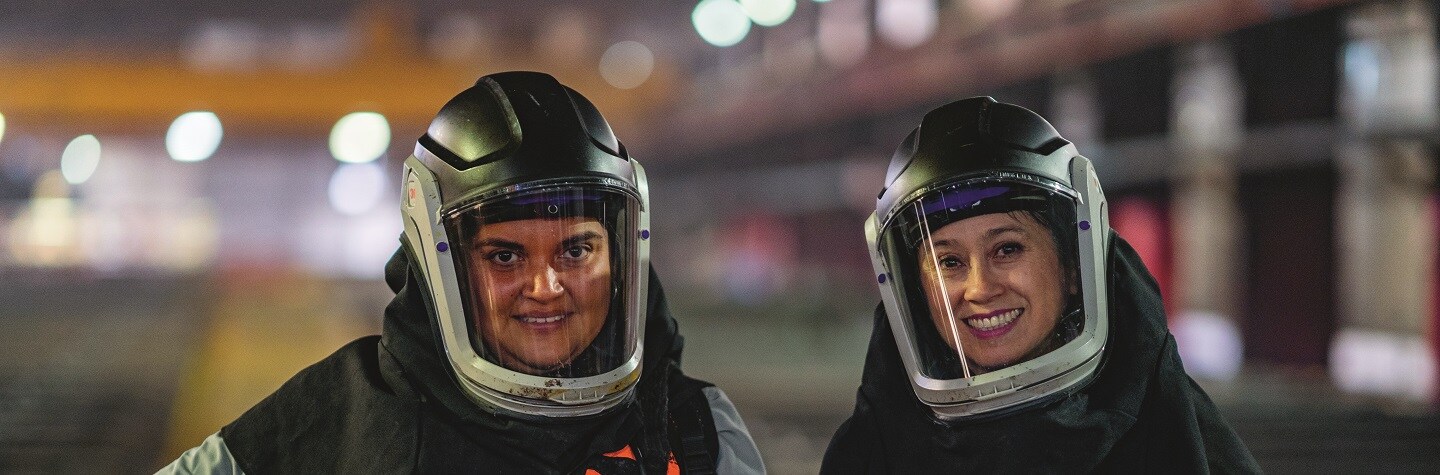 Two women in protective equipment stand next to each other, smiling.