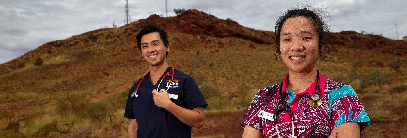 Two new GPs stand smiling, with Newman in the background