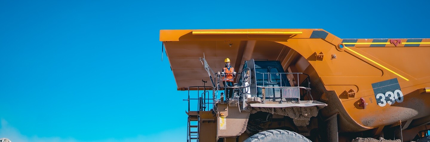 A woman stands on a yellow truck with blue sky in the background