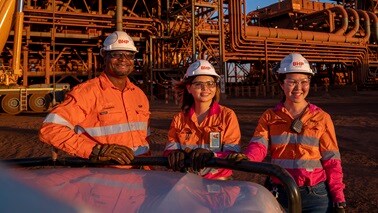 Three people in BHP orange shirts and hard hats outside processing facility