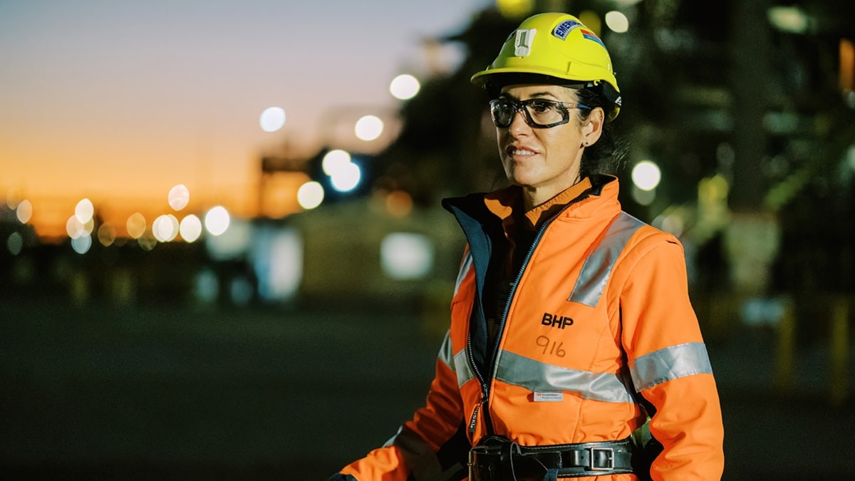 Woman standing at front of Olympic Dam with lights and dusk shown in the background