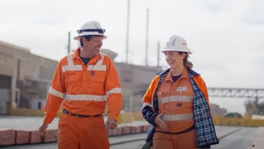 Man and woman shown walking along in BHP orange PPE and smiling