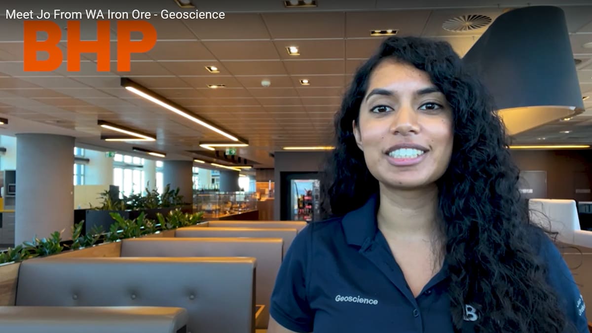 Woman is pictured in a BHP Geoscience shirt sitting in collaboration area smiling