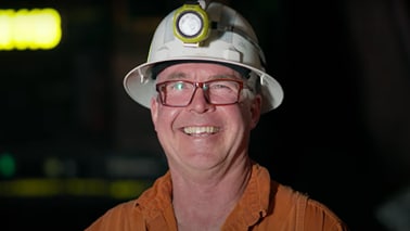 Man in BHP orange shirt and hard hat, shown underground with light on his helmet, smiling 