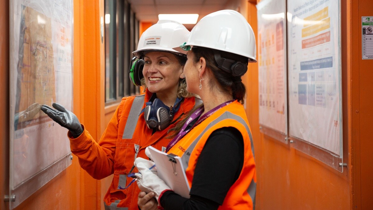 Two women shown wearing BHP PPE and smiling reading health and safety boards with map of Chile 