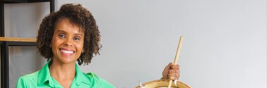 Luciana shown smiling with drums, wearing a green shirt