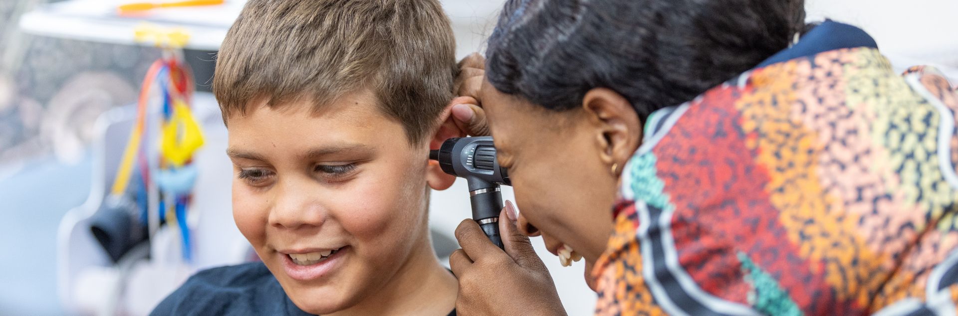Healthcare professional uses an otoscope to examine a young child’s ear in a clinical room