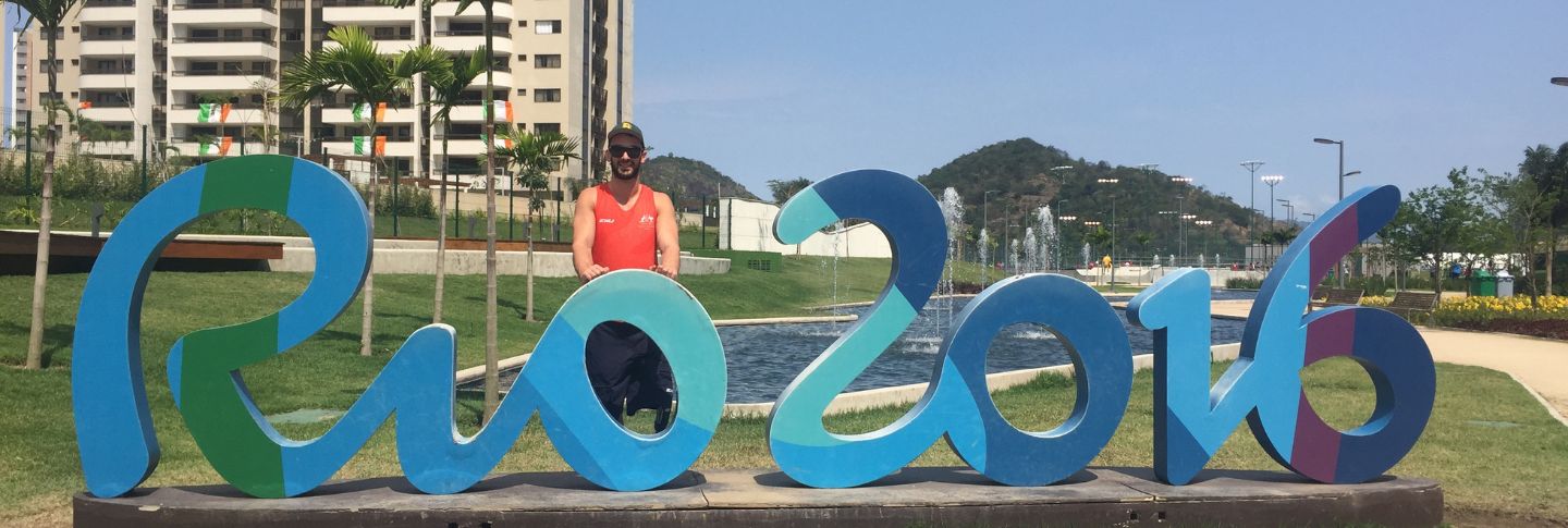 man in wheelchair in front of a rio 2016 sign 