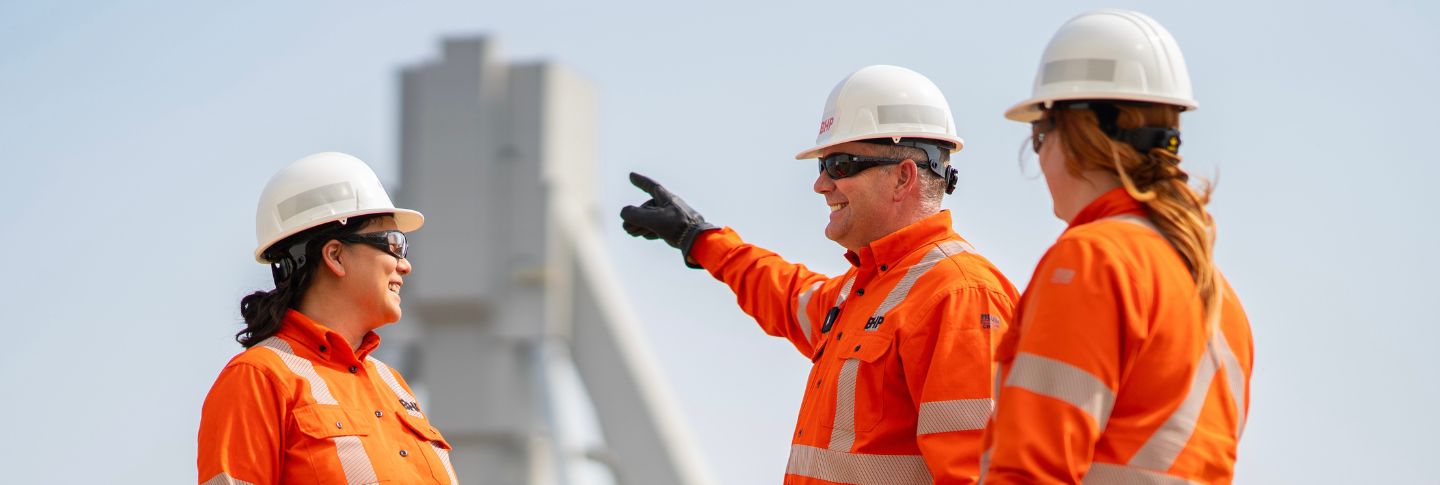 man and three women in mining uniform man pointing at Jansen mine in background