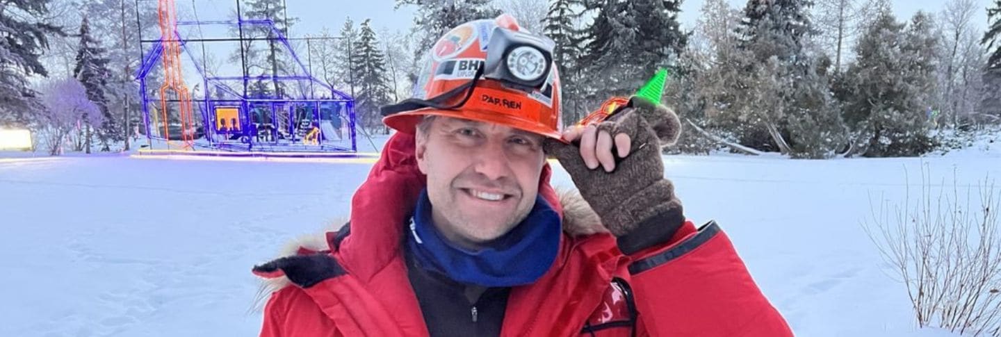 man in the snow smiling to camera with mining hard hat on