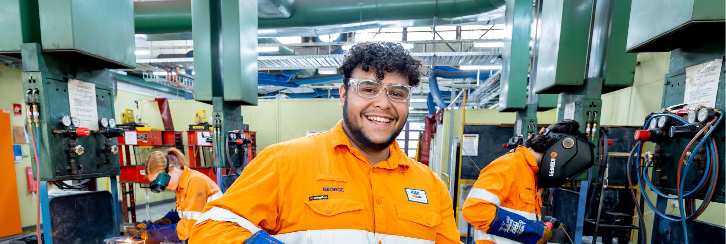 young male apprentice in a workshop wearing a mining uniform and glasses