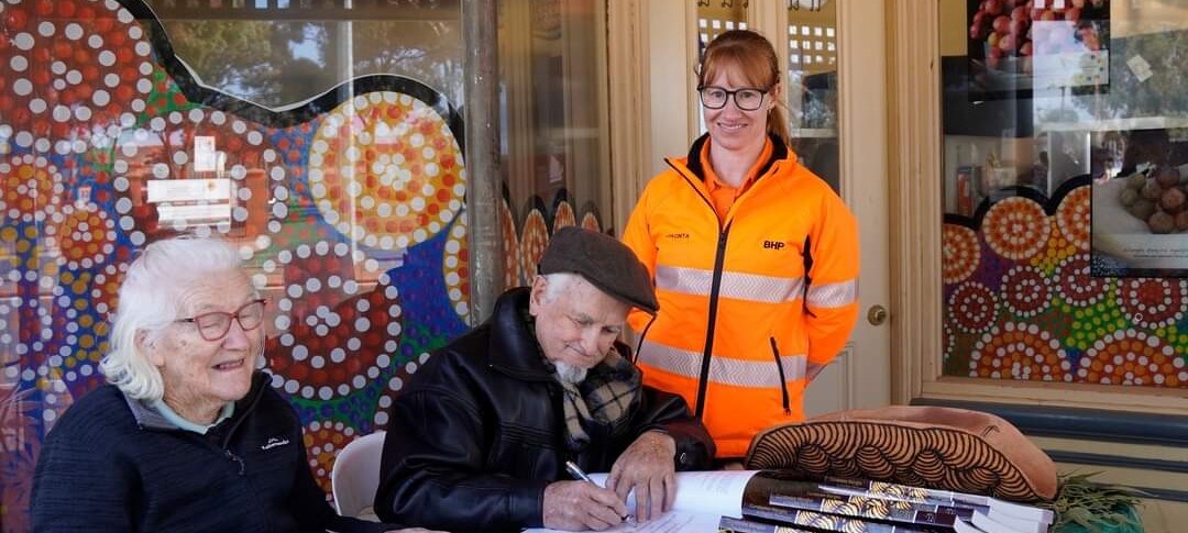 elderly man and woman at a table sitting woman in high vis standing smiling to camera
