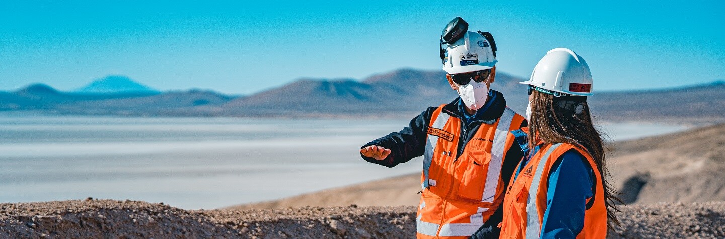 Two people in PPE look out over a tailings facility