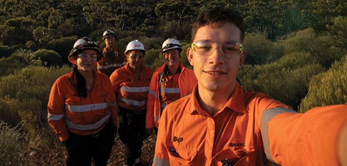 APPRENTICES IN A FIELD ONE PERSON TAKING PHOTO FOUR BEHIND HIM IN PPE GEAR
