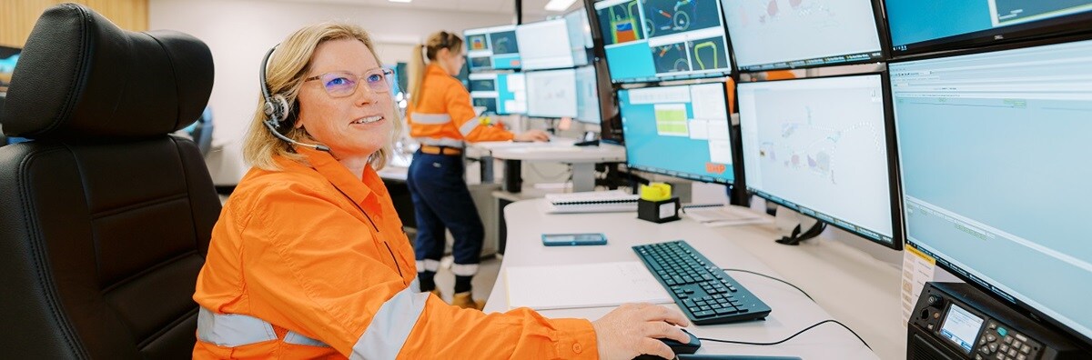 A woman sits smiling, looking at multiple computer screens. 
