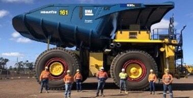 workers in front of giant yellow mining truck with blue tray