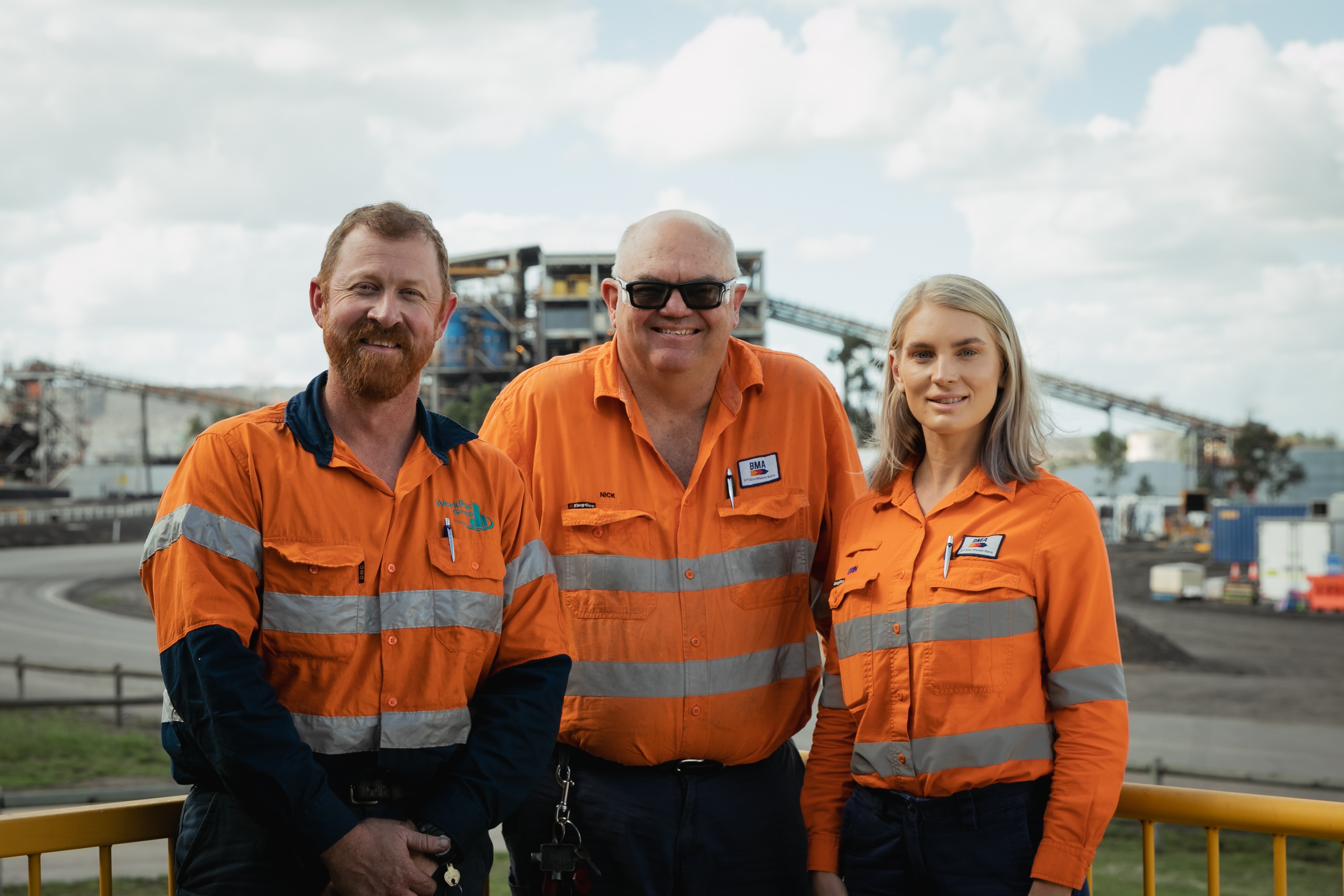 two men and a woman standing smiling to camera on a mine site