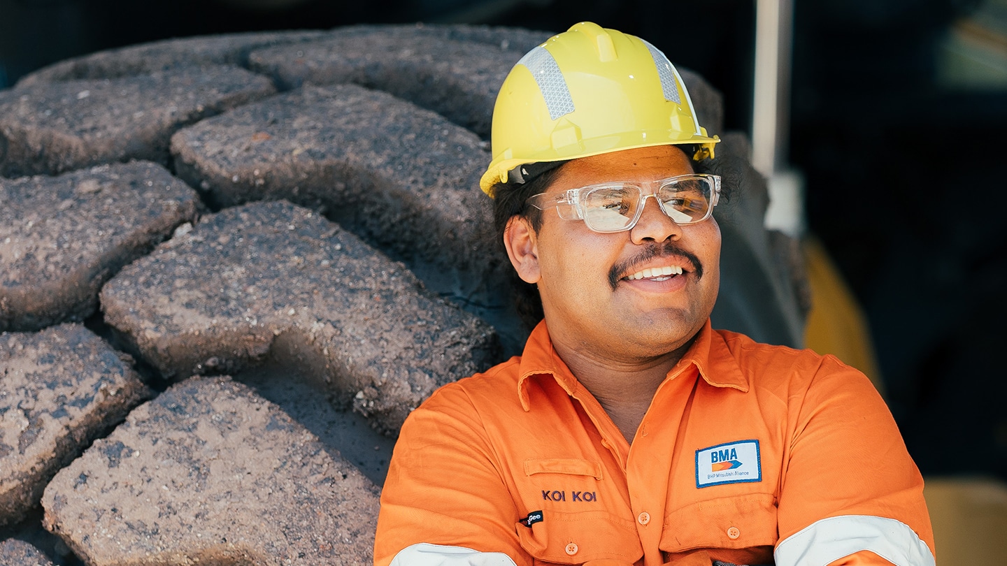 Koi Koi in BMA short standing behind large tire and smiling 