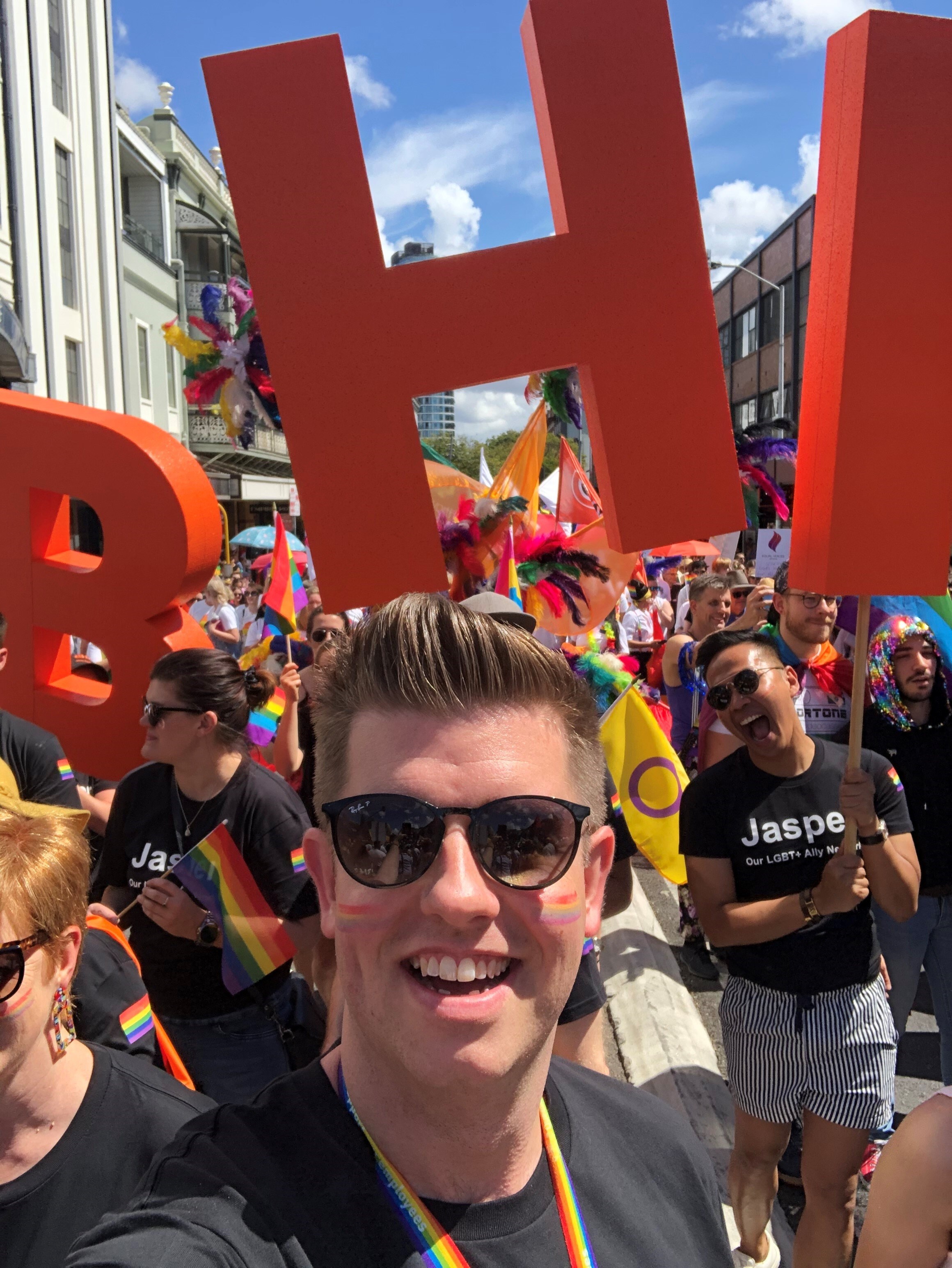 man smiling to camera at a pride parade in a crowd