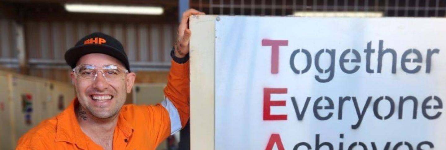man smiling to camera at a sign that says team